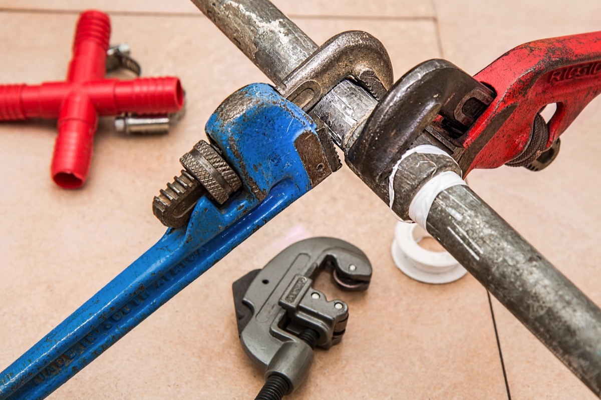 RIDGID pipe wrenches and a tube cutter laid out on a tile floor, representing the professional plumbing tools required for gas tankless water heater installation and service