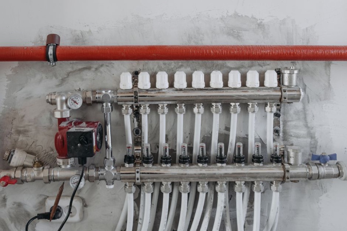 Red-bodied circulation pump mounted on a home plumbing manifold with multiple copper and PEX pipe connections, illustrating how recirculation integrates into a water distribution system