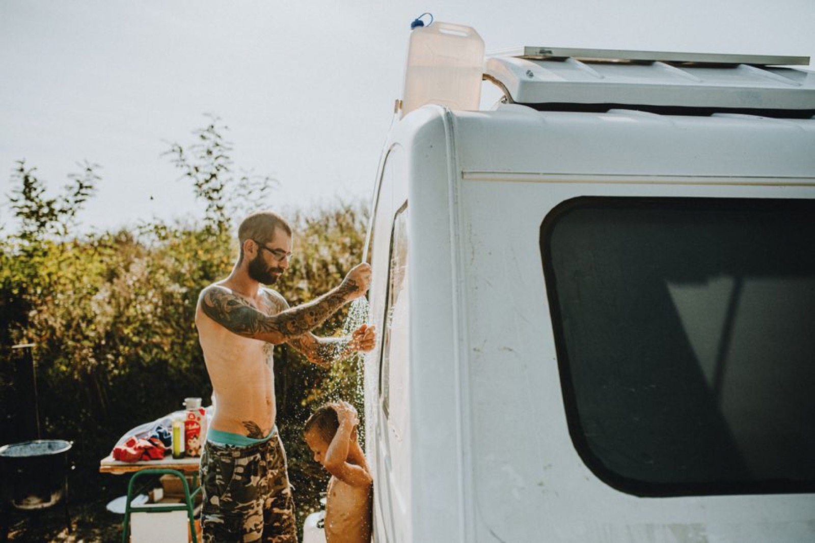Father and son taking an outdoor shower next to their campervan during a summer camping trip