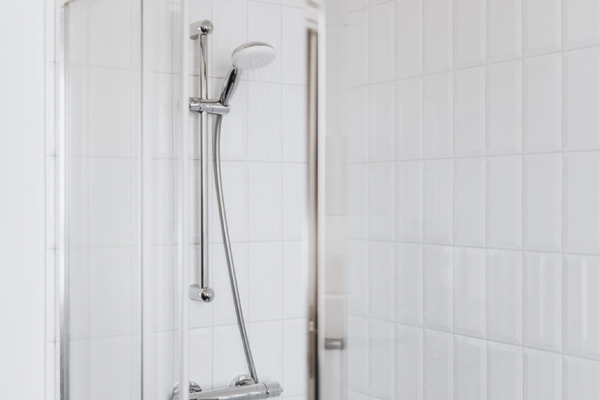 White-tiled shower with chrome thermostatic mixing valve and handheld shower bar, showing a clean single-wall in-wall valve installation