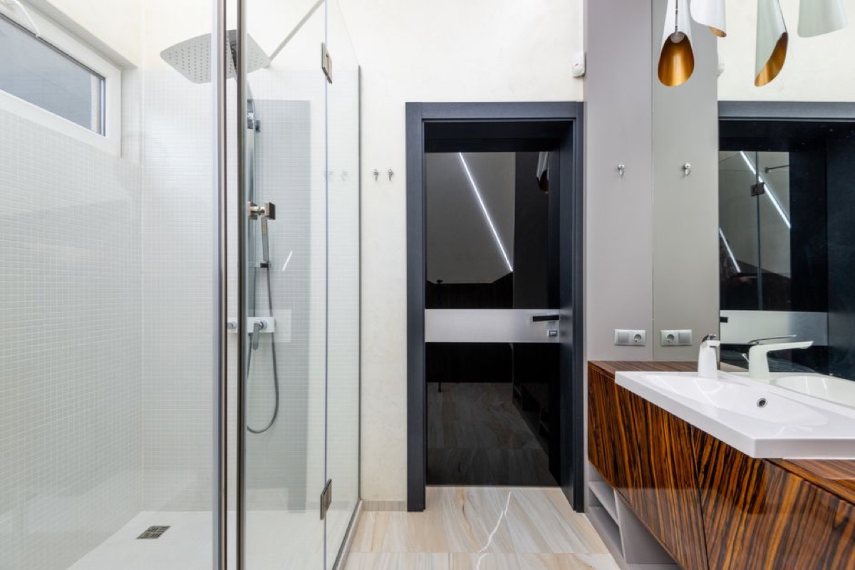 Modern bathroom with glass-enclosed shower featuring a large rain head and handheld shower fixture, showing a two-fixture setup requiring a diverter valve