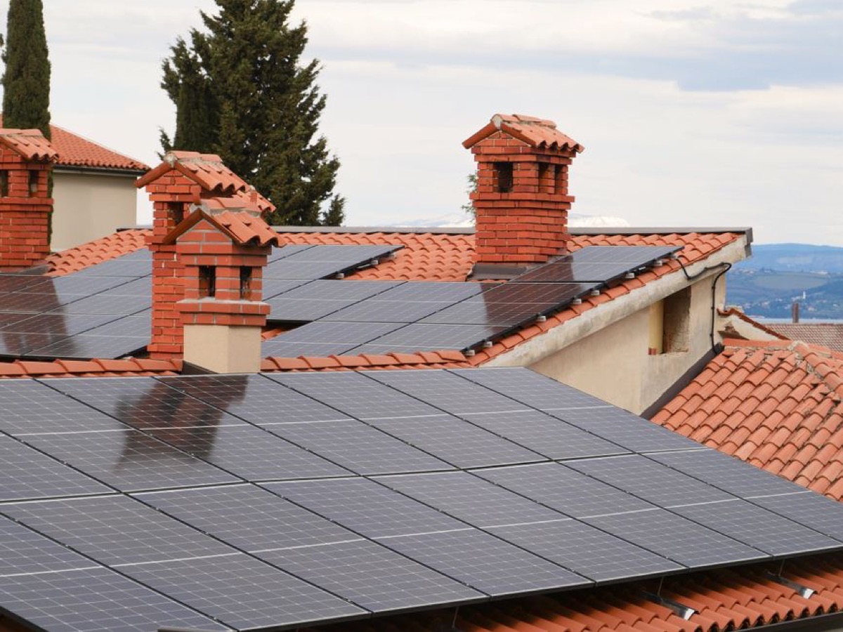 Solar collector panels on tiled residential rooftop with chimneys, showing a typical residential solar thermal installation for water heating preheat systems