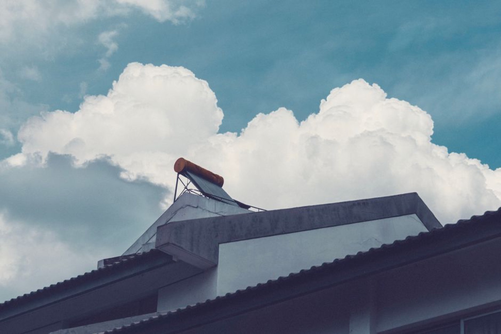 Solar water heater collectors mounted on a residential rooftop against a bright sky, representing solar thermal preheat systems paired with tankless water heaters