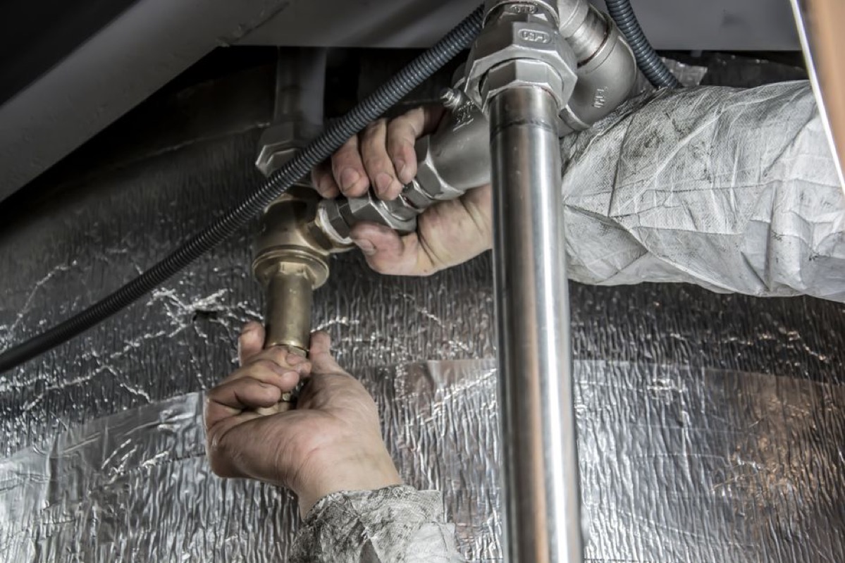 Plumber's hands working on insulated steel pipes, showing pipe insulation installation technique for freeze protection