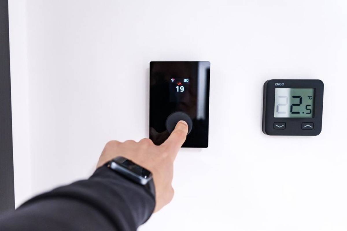 Hand adjusting digital thermostat controls, illustrating energy efficiency improvements that qualify for the IRS 25C tax credit